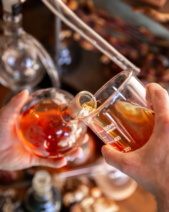 Pouring a dual-extracted tincture between glass vessels